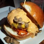 Burger with cheddar, mushrooms, and roasted peppers on a brioche bun.